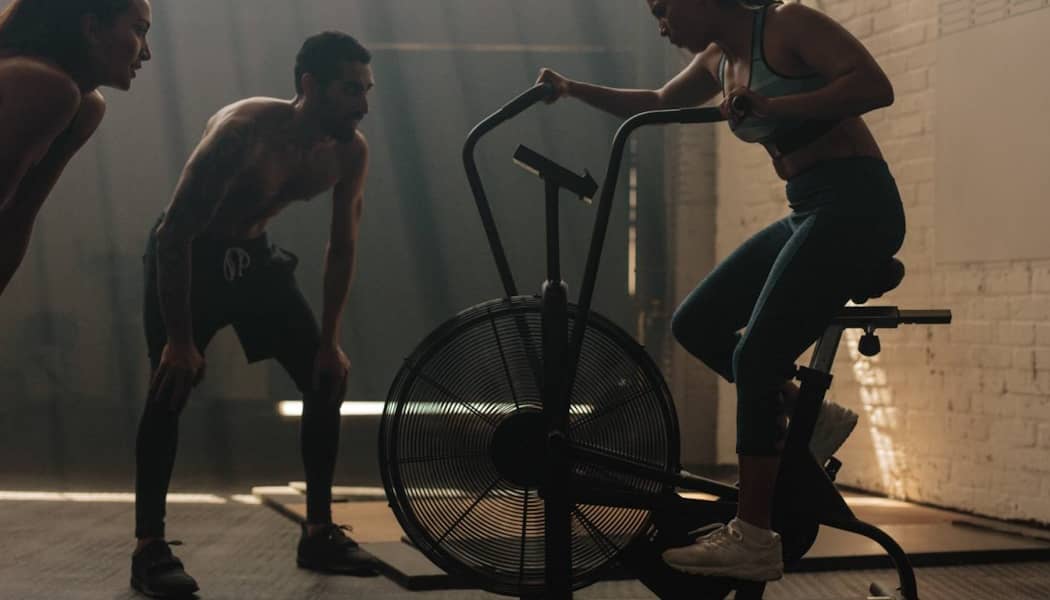 A woman using an indoor spin bike being encouraged by two others